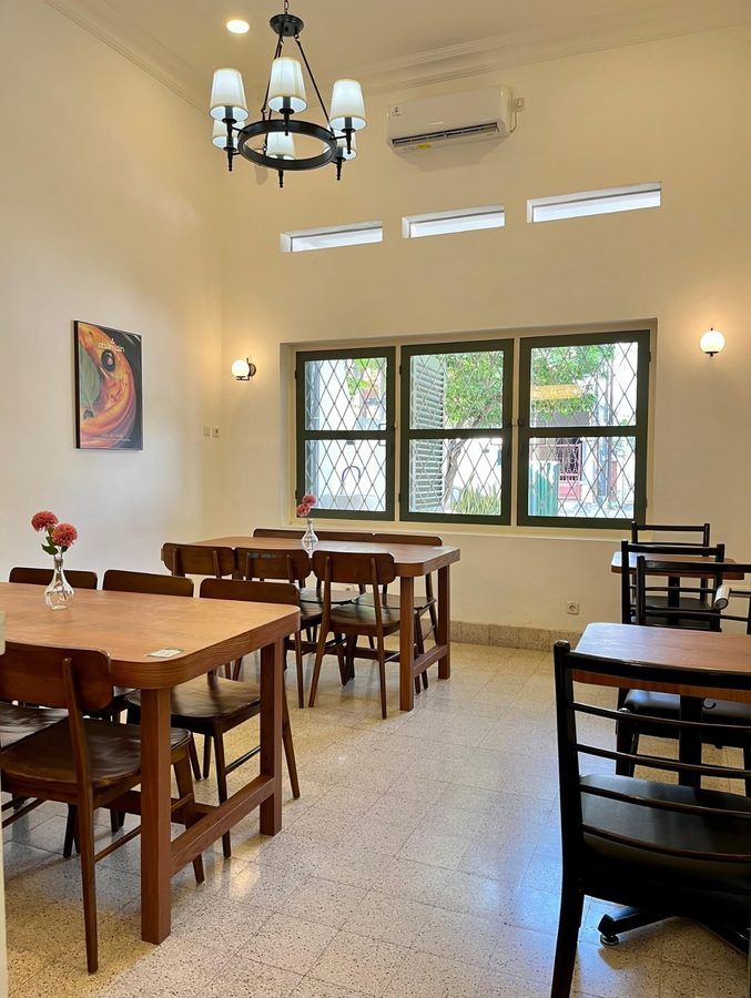 Sudut duduk Abumain Bake and Bistro dengan meja kayu dan lukisan croissant